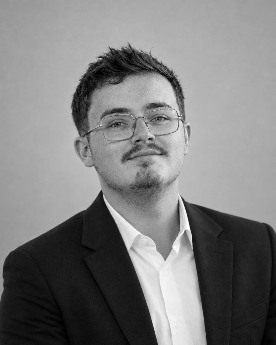 Portrait en noir et blanc de Simon Beuvain, lunettes fines, veste sombre et chemise blanche